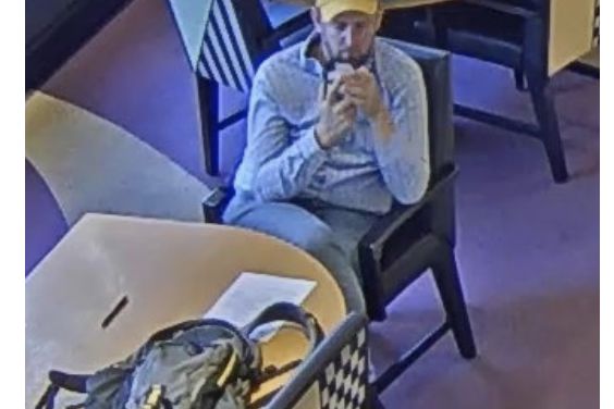 A surveillance photo of a man sitting inside a bank wearing a yellow baseball cap.